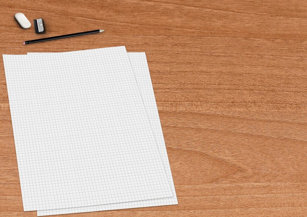 Blank grid paper with a pencil, eraser and sharpener on a wooden desk
