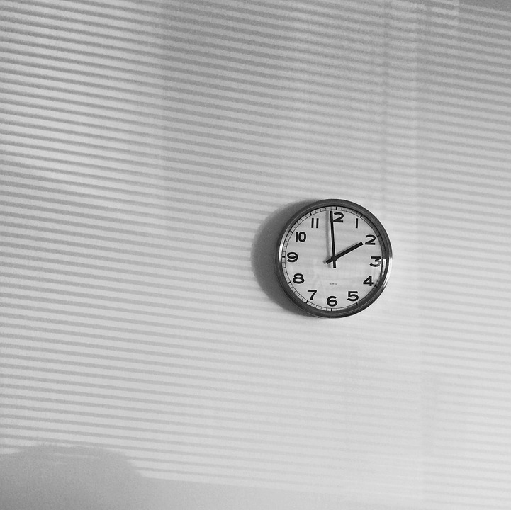 A simple wall clock lit by light through window blinds
