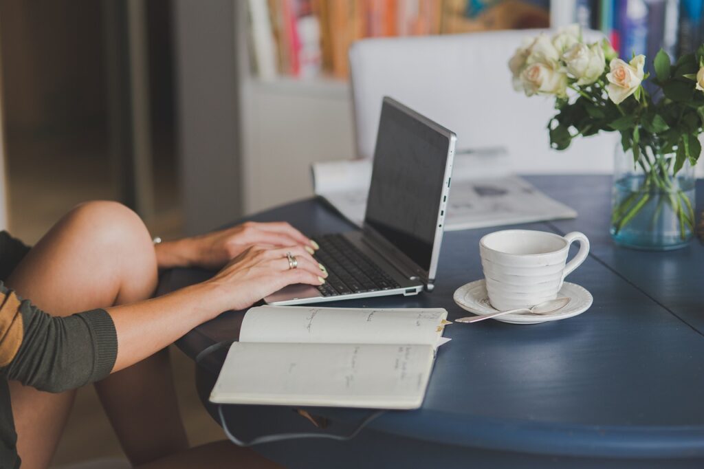 A person typing a customer email on a laptop at a table with a notebook and coffee